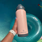 Person holding a pink and black insulated bottle with 'hydrate better' branding near a pool.